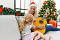 Mother and daughter playing guitar and singing sitting by christmas tree at home Royalty Free Stock Photo
