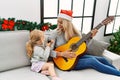 Mother and daughter playing guitar and singing sitting by christmas tree at home Royalty Free Stock Photo