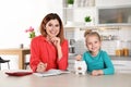 Mother and daughter putting coin into piggy bank at table indoors. Royalty Free Stock Photo