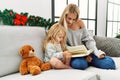 Mother and daughter reading book sitting by christmas decor at home Royalty Free Stock Photo