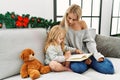 Mother and daughter reading book sitting by christmas decor at home Royalty Free Stock Photo