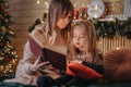 Mother and daughter reading fairytales during Christmas eve, wonderful atmosphere of love and trust, belief in miracles.