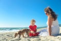 Mother and daughter in red dress and dog on the beach Royalty Free Stock Photo