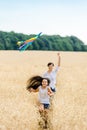 Mother and daughter run in a wheat field with a kite in the summer. Well-planned and active weekend. Happy childhood. Royalty Free Stock Photo