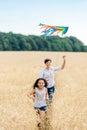 Mother and daughter run in a wheat field with a kite in the summer. Well-planned and active weekend. Happy childhood. Royalty Free Stock Photo