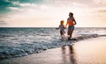 Mother and daughter running along the seashore at sunset - Happy family having fun playing together in vacation on the beach Royalty Free Stock Photo