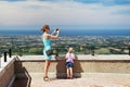 Mother with daughter at San Marino observation deck. Mom taking landscape photo with smartphone. Child looking at italian coast o