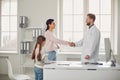 Mother with daughter shakes hands with the doctor standing in the clinic office in the clinic office.