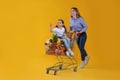 Mother and daughter with shopping cart full of groceries on yellow background Royalty Free Stock Photo