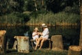Mother and daughter sitting on bench next to stumps on background of river