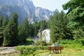 A mother and daughter sitting on a bench on the ocean in front of a waterfall, forests and a giant rock face behind her Royalty Free Stock Photo