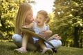 Mother and daughter sitting on green grass and reading book together. Little girl sitting on mother lap. Royalty Free Stock Photo