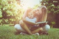 Mother and daughter sitting on green grass and reading book together. Little girl sitting on mother lap. Royalty Free Stock Photo