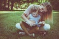 Mother and daughter sitting on green grass and reading book together. Little girl sitting on mother lap. Royalty Free Stock Photo