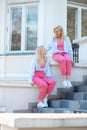 Mother and daughter sitting near stairs and laughing. Mom straighten white hair of girl. Funny talk between relatives.