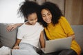 Mother and daughter sitting on sofa at home using laptop.