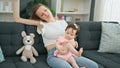 Mother and daughter sitting on sofa tired stretching arm at home