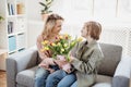 Mother and daughter sitting on the sofa with tulips in their hands indoor. Royalty Free Stock Photo