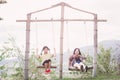 Mother and daughter sitting on a swing under tree on a warm summer evening while swaying in sunlit nature.Happy mom and daughter