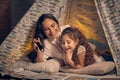 Mother and daughter are sitting in a teepee tent, reading stories with the flashlight. Happy family. Royalty Free Stock Photo