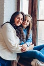 Mother and daughter sitting on window sill hugging looking at camera. Family time Royalty Free Stock Photo