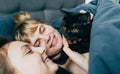 Mother and daughter sleeps together in a bed with a black cat. Family spending time together. Close up portrait of smiling woman h Royalty Free Stock Photo