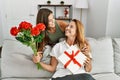 Mother and daughter smiling confident holding gift and flowers at home