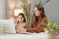 Mother-daughter study time. Home education support. Concentrated focused little girl with teacher using laptop while sitting at Royalty Free Stock Photo