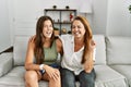 Mother and daughter together sitting on the sofa at home winking looking at the camera with sexy expression, cheerful and happy Royalty Free Stock Photo
