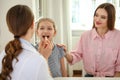 Mother and daughter visiting pediatrician. Doctor examining little patient`s throat Royalty Free Stock Photo