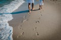 Mother and daughter walking on beach leaving footprint in sand