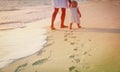 Mother and daughter walking on beach leaving footprint in sand