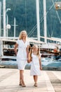 Mother and daughter walking by the harbor and marina with yachts in a touristic luxury sea resort. European summer vacation.