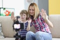 Mother and daughter wave hello on video, videocamera set on tripod