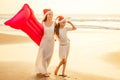 Mother and daughter in white dress and red Santa Claus hat having fun walking by summer sunset beach with air mattress Royalty Free Stock Photo