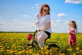 Mother and daughter wtht a bicycle in a field with yellow dandelions. Family walks in the spring in nature Royalty Free Stock Photo