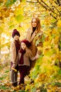 Mother with daughters in autumn park under yellow maples. happy family