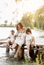 Mother day. Happy young mom with little girls sitting on wooden bridge near lake, pond on summer. Mother and two child Royalty Free Stock Photo