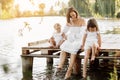 Mother day. Happy young mom with little girls sitting on wooden bridge near lake, pond on summer. Mother and two child Royalty Free Stock Photo