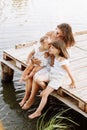 Mother day. Happy young mom with little girls sitting on wooden bridge near lake, pond on summer. Mother and two child Royalty Free Stock Photo