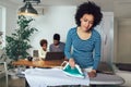 Mother doing hosehold chores and ironing, family are in background