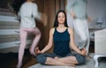 Mother doing yoga meditation exercise indoors at home, daughters playing.