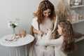 A mother in a dress sits in a chair and plays with her daughter