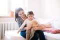 Mother dressing her daughter in the morning on a couch