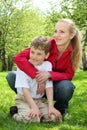 Mother embraces behind son sitting in lap on grass