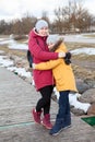 Mother embracing her frozen daughter, adult woman and young girl stand on quay at winter cold weather, people dressed warm clothes