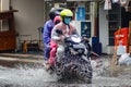a mother, father and child as a family ride a motorbike wearing raincoats through floodwaters during heavy rain