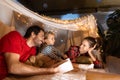 Mother, father and daughter lying inside self-made hut, tent in room in the evening and reading book. Having fun Royalty Free Stock Photo