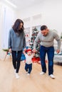 Mother and father holding their cute baby by hands and teaching him how to walk in the middle of the christmas decorated Royalty Free Stock Photo