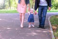 Baby girl trying to go making first steps holding mom dad`s hands in city park. Royalty Free Stock Photo